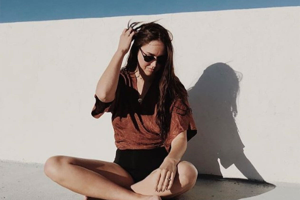A seated woman wearing sunglasses wearing black shorts and brown top from Cub Clothing, one of Toast's ethical Canadian fashion brands