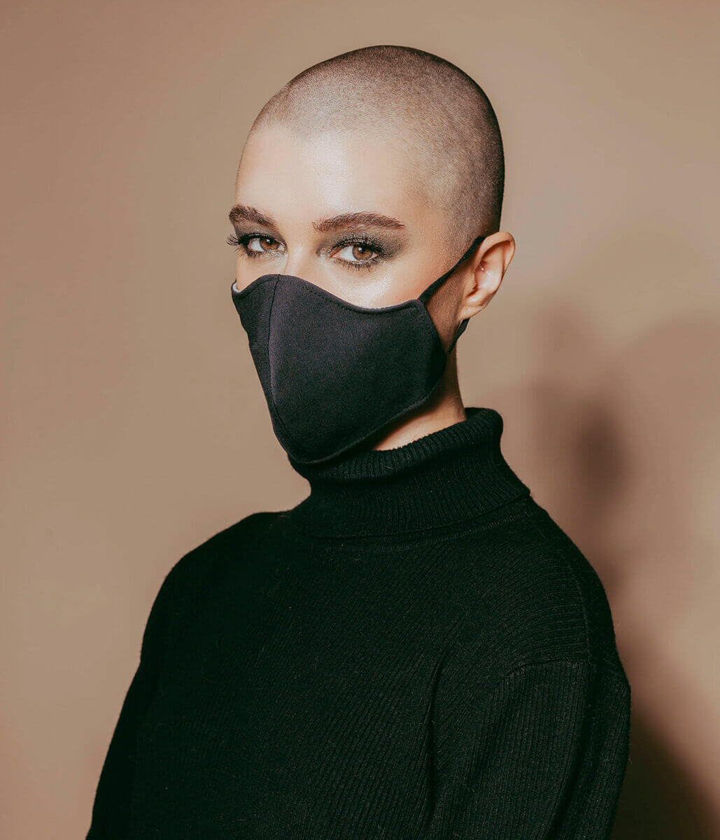 Woman with shaved head in black sweater with black mask, wearing mask-friendly minimal makeup 