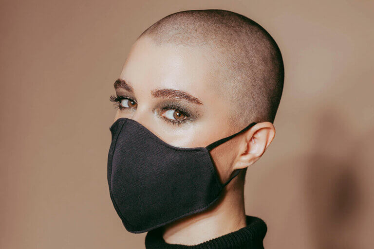 Woman with shaved head wearing a mask and minimal makeup