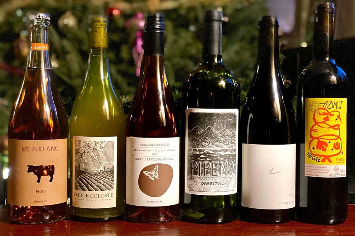 A row of six red and white wine bottles, all sustainably-farmed natural wines