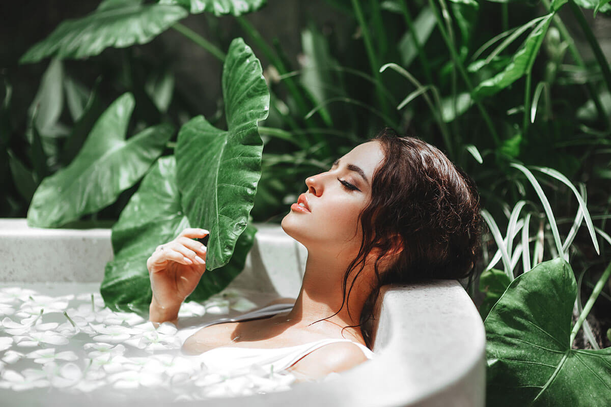 Toast wellness trends for 2021 include mind and body bathing, and here a woman soaks in a tub surrounded by greenery.