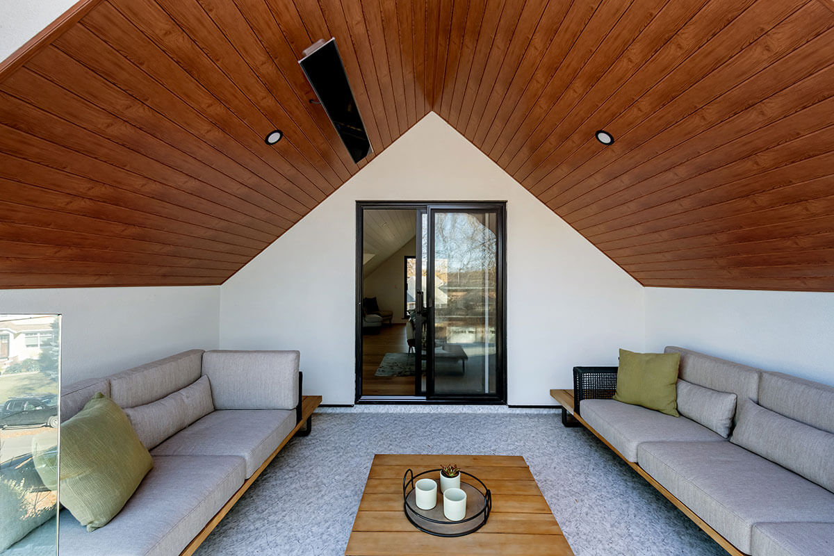 An outdoor living space attached to a house with wood ceiling, couches and ceiling heater 