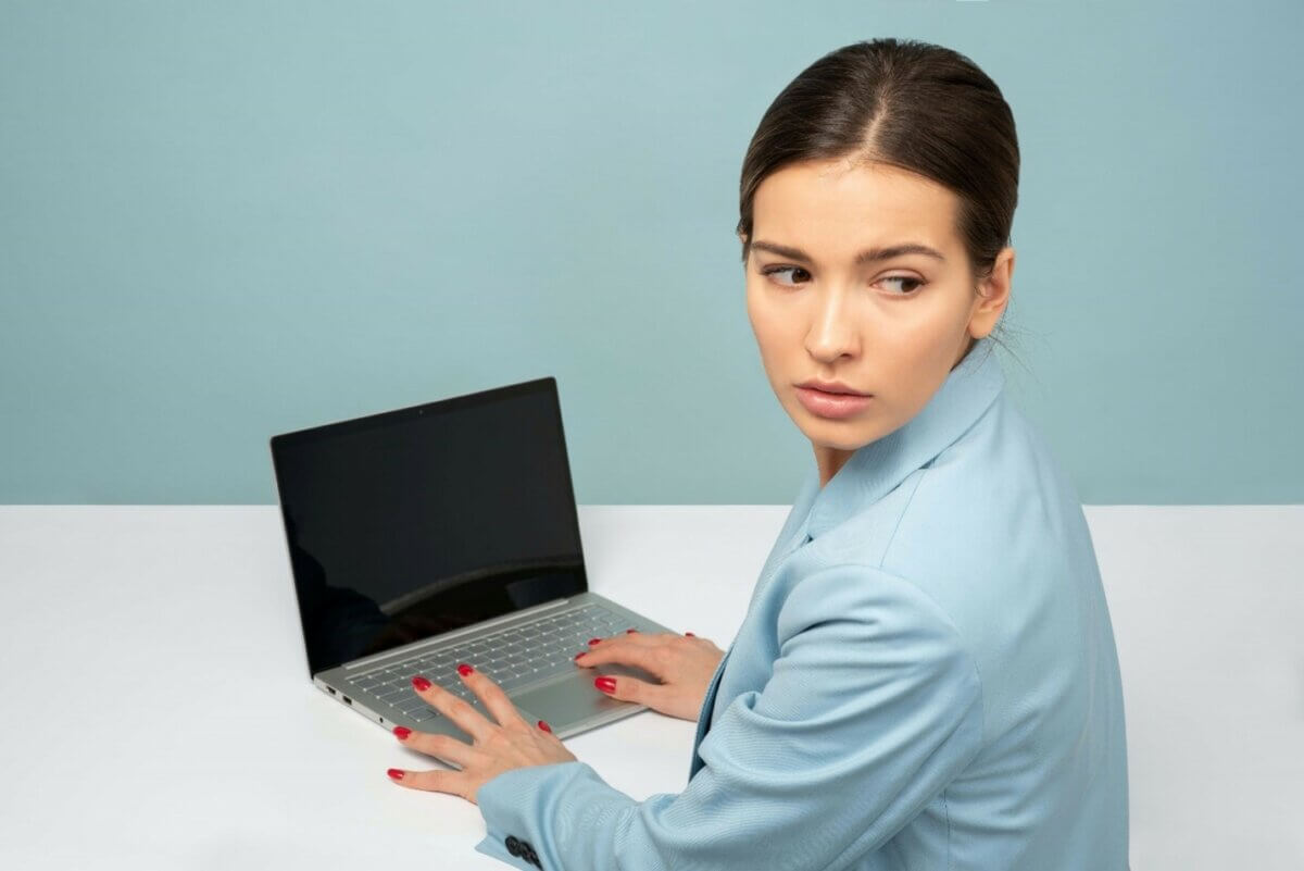 woman in a blue suit at a computer looking over her shoulder in worry, committing financial infidelity