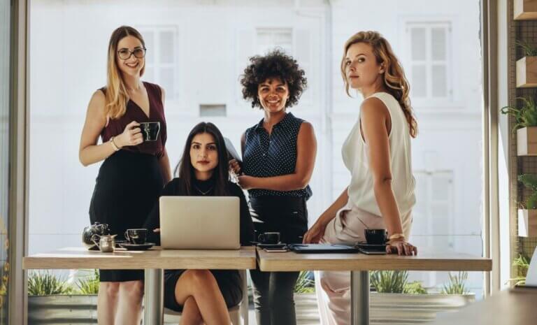 four businesswomen standing and sitting at a desk