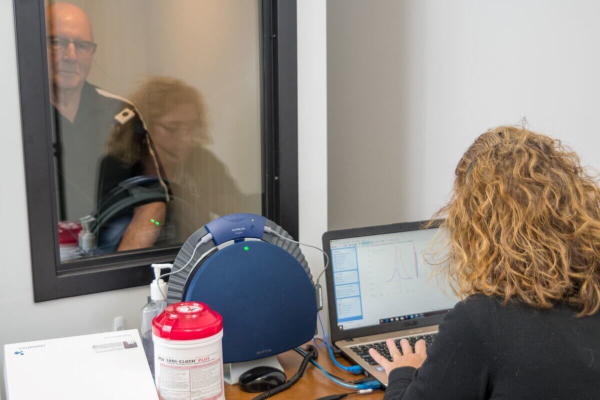 A hearing practitioner running a hearing loss test on a man in a sound booth