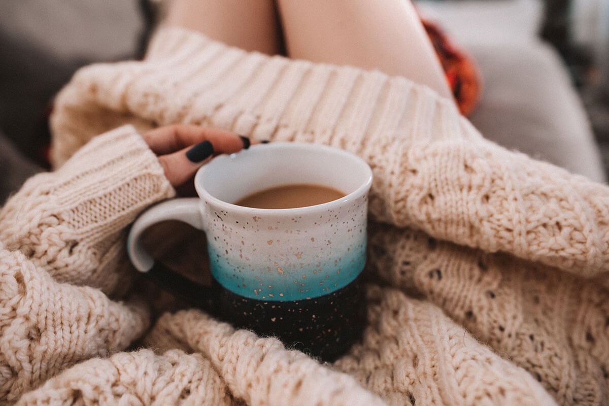 The Hygge life, part of a woman's body showing a pink sweater and a hand holding a cup of coffee