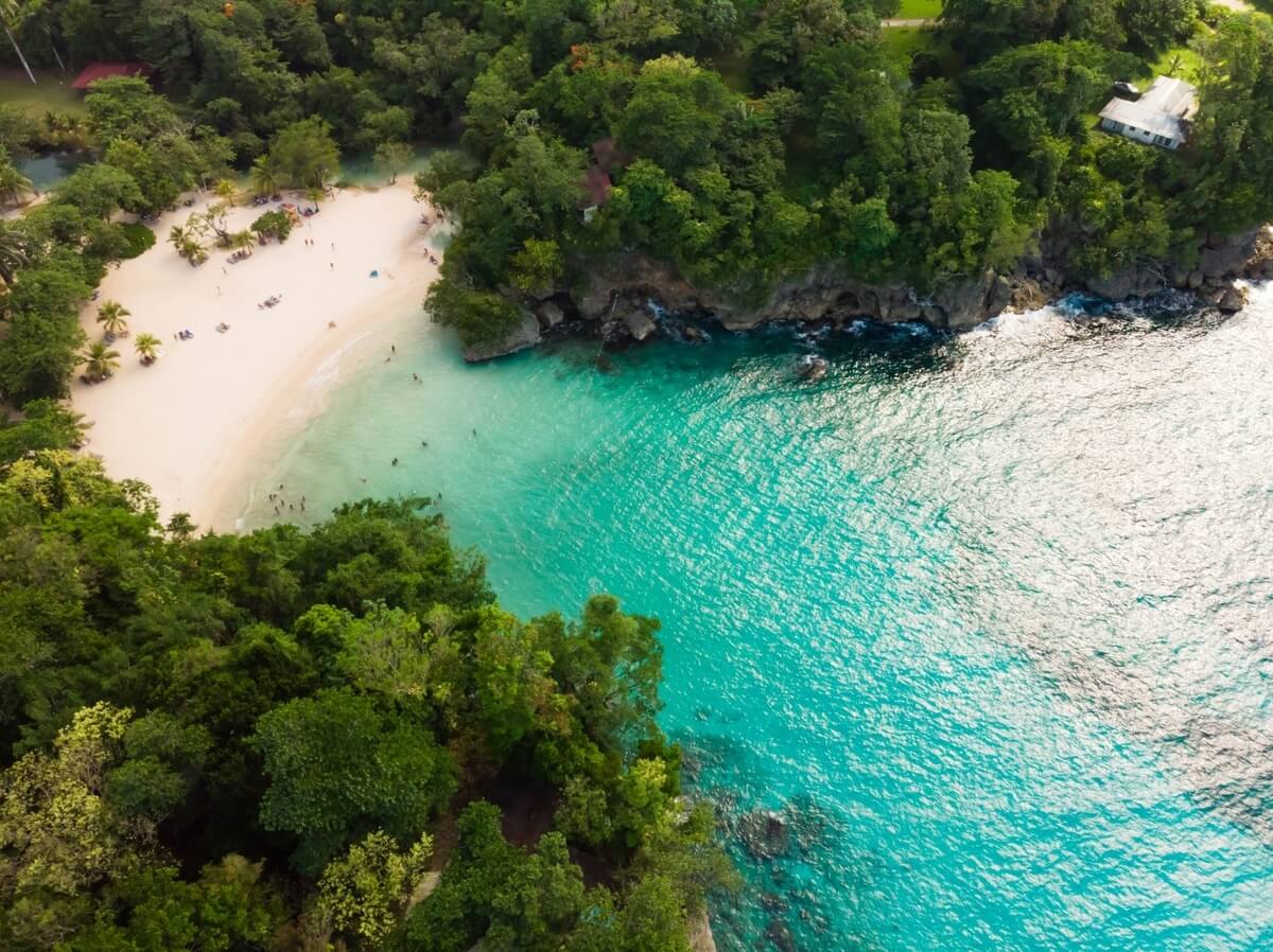 A view from above of a Jamaican beach tucked inside a treed cove with turquoise blue water, part of Jamaica's one-love treasures