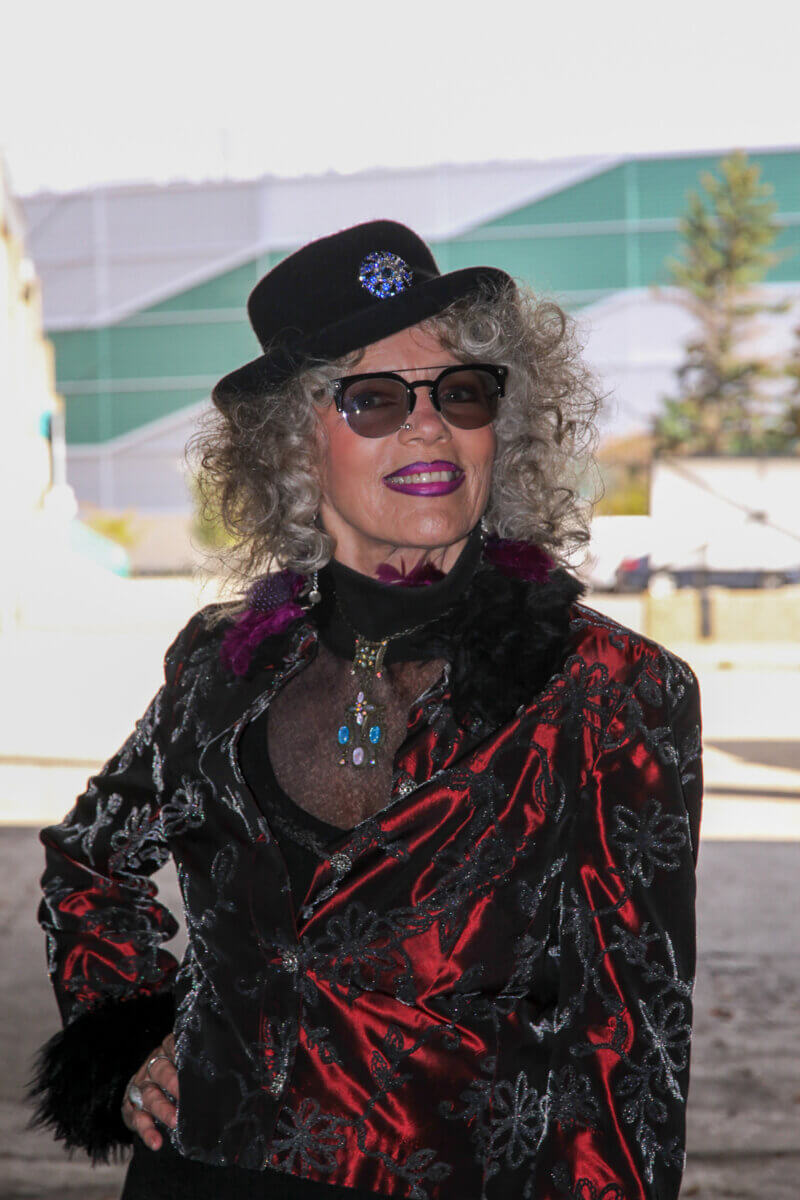 A vibrant woman in her 70s living out loud, modelling a black and red jacket with black hat and sunglasses