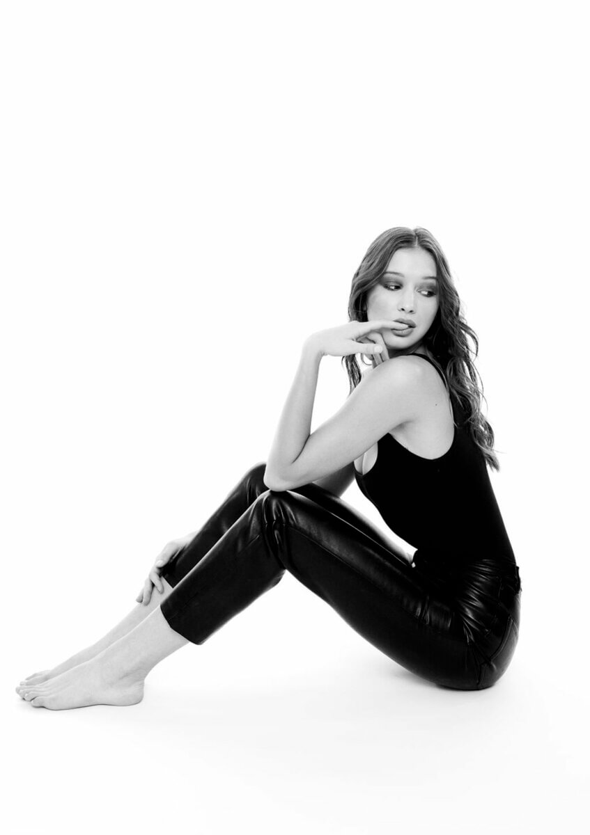 A seated young woman wearing black pants and black tank top, one of a few monochromatic looks by Nicole Romanoff