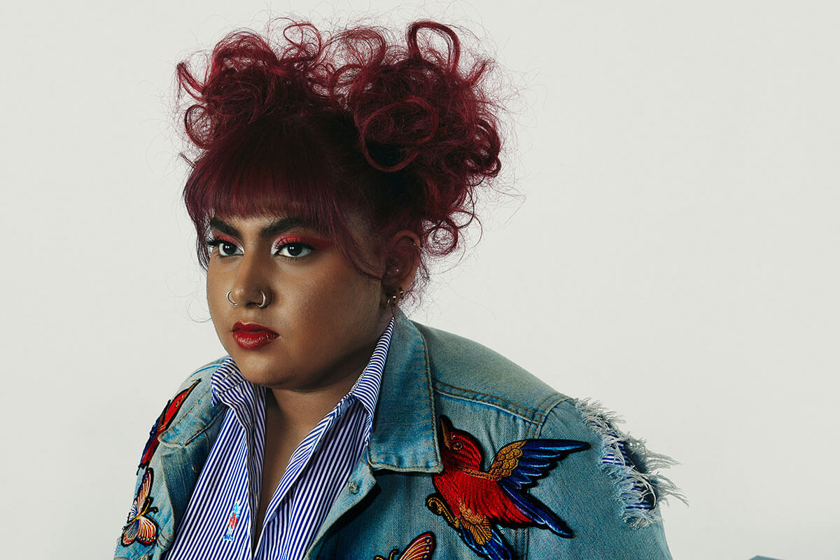 rising Canadian artist, Nisha Patel in a jean jacket and red hair