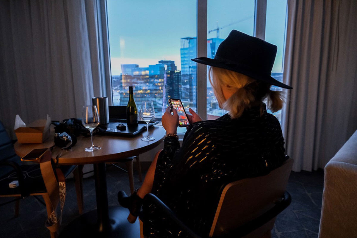 A woman sitting in her hotel room with a glass of wine, looking out over the city