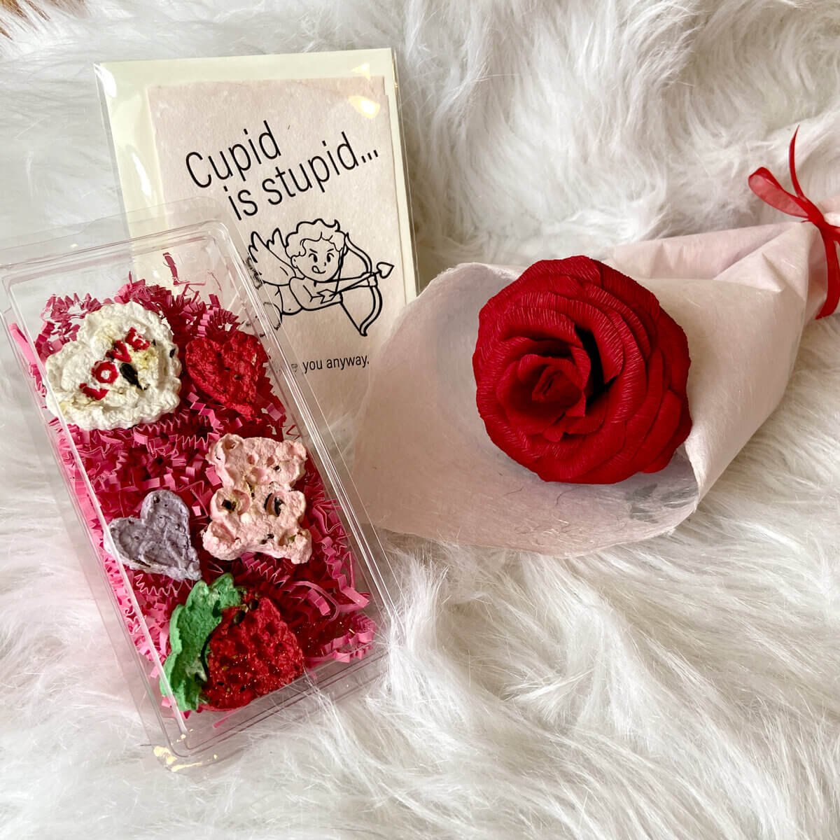 A rose, a case of colourful paper-made gifts and a Cupid card on a white furry background
