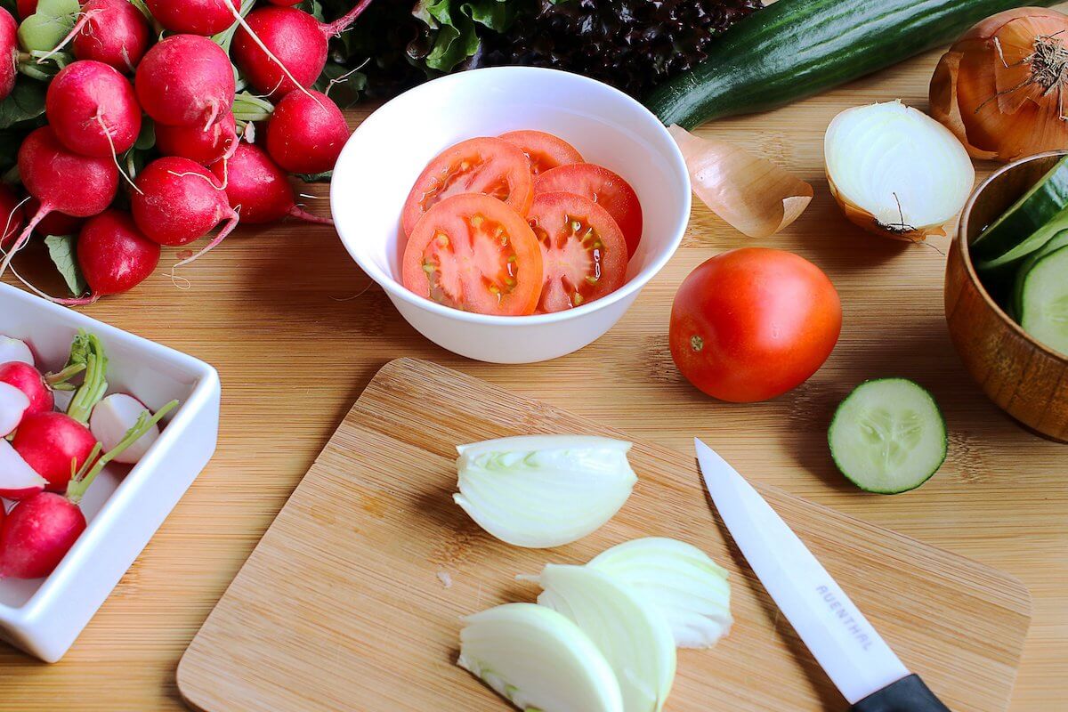 cut vegetables on a board including tomatoes, onions, cucumber and radishes, eating healthy with an air fryer