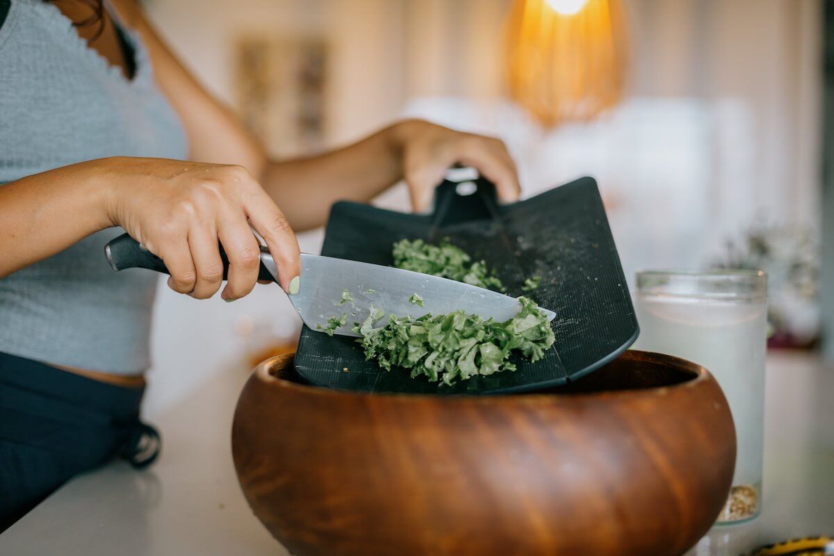 chopped kale being scraped into a wooden bowl, ingredients for air fryer