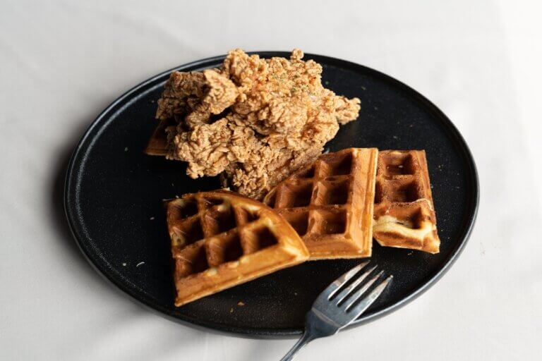 piece of fried chicken, cooked in an air fryer, and waffles on a black plate
