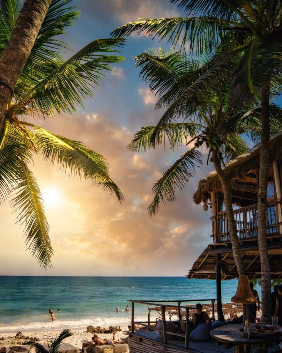 A beach hut, palm trees and people swimming, part of Cancun adventures