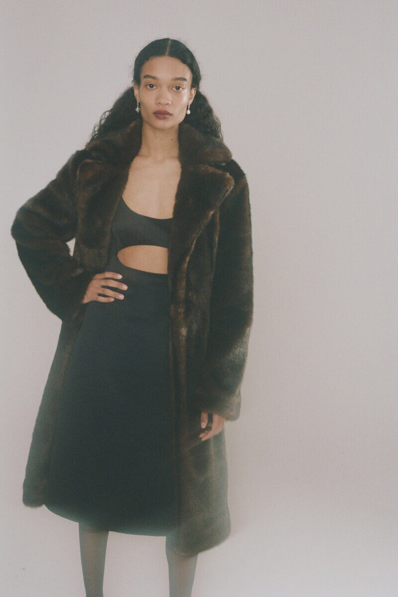 Standing model in black dress & long brown fur coat by Sandy Liang RTW