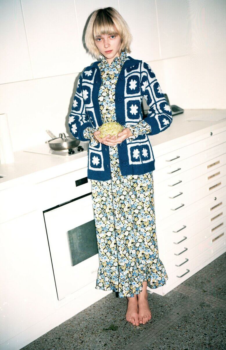 Model in a kitchen wearing a long floral dress with a blue & white knit cardigan sweater, by Batsheva RTW Fall 2021 fashion collections