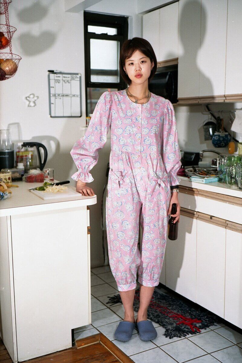 Woman in kitchen wearing pink floral pajama-style jumper, by Batsheva RTW Fall 2021 fashion collections