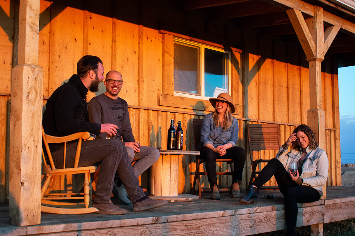 2 women and 2 men sitting outside by a wooden building, owners of odla committed to farmr to table dining