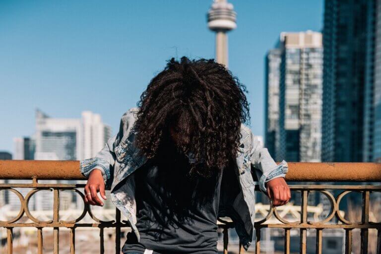 A person standing beside a bridge wearing a jean jacket and casual clothes to found at indie boutiques in Toronto