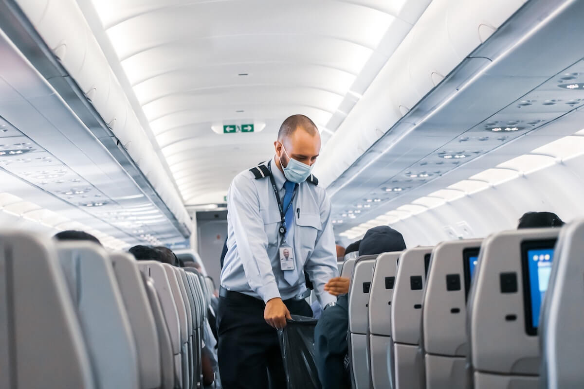 Airline attendant gathering garbage on a flight, part of post-COVID vacation safety