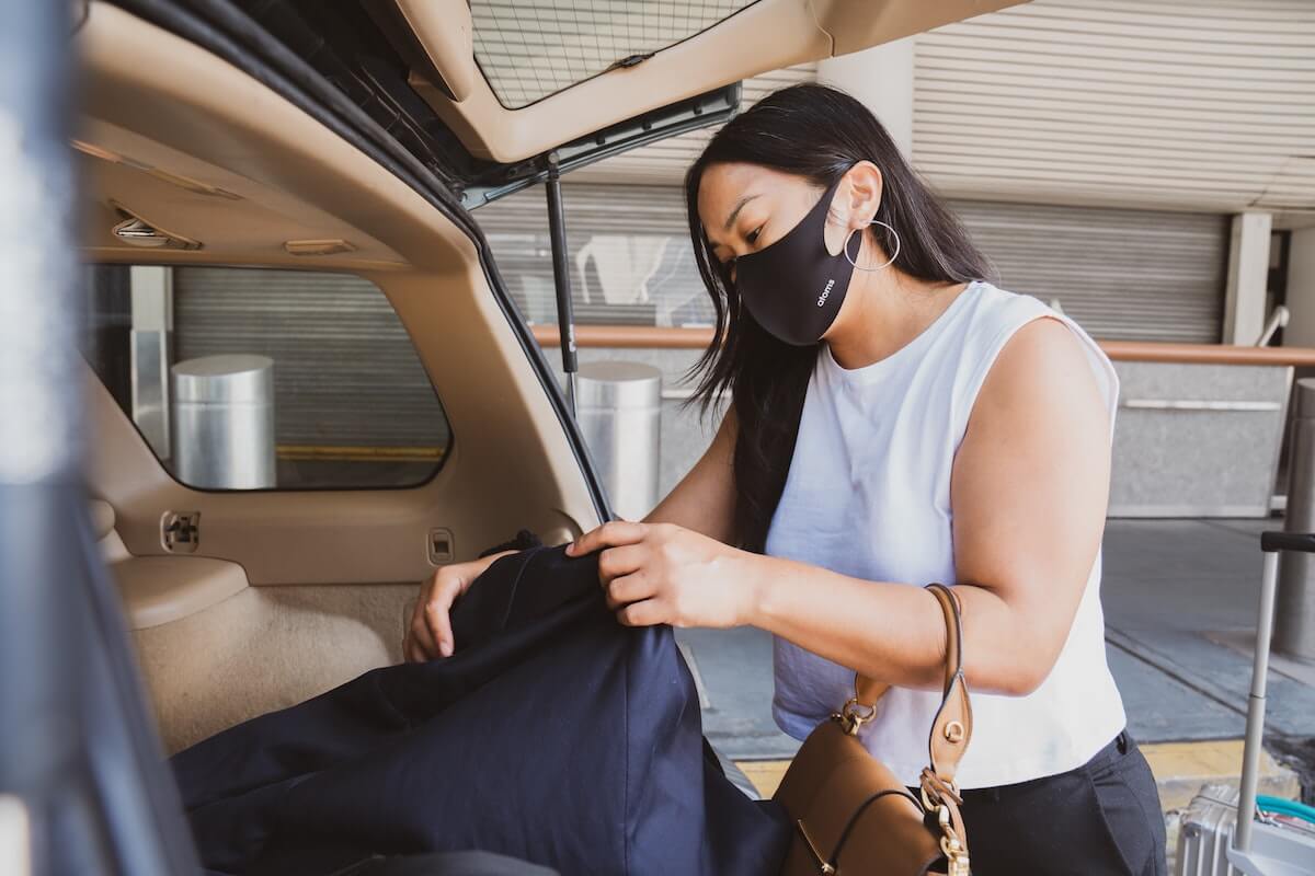 A woman removing her luggage from a vehicle and following post-COVID vacation safety