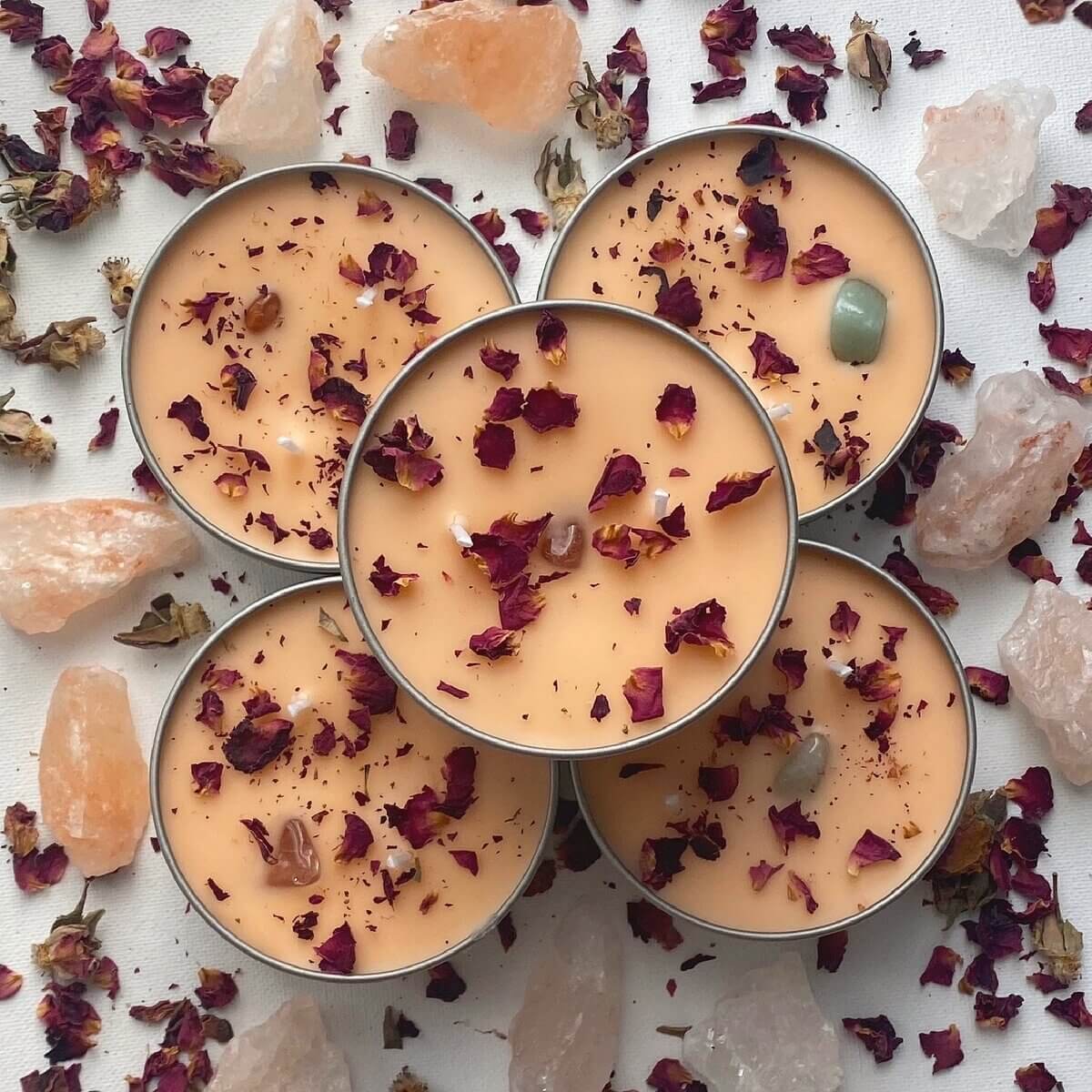 5 peach coloured round candles with red leaves surrounded by crystal salt stones