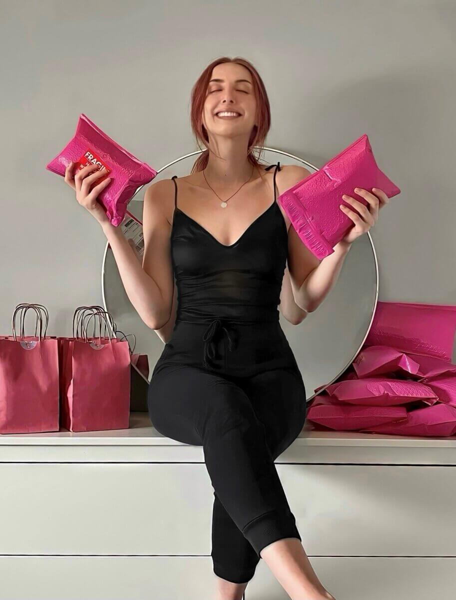 a seated smiling woman with eyes closed holding pink packaged candles near pink bags 
