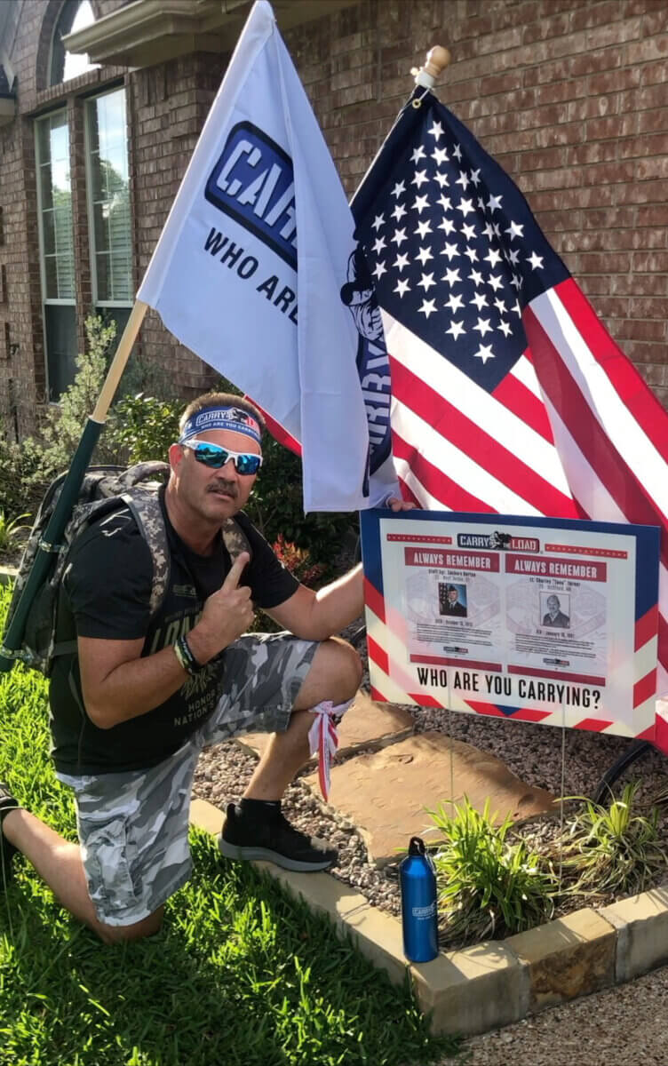 man kneeling beside a US flag at a carry the load memorial day march