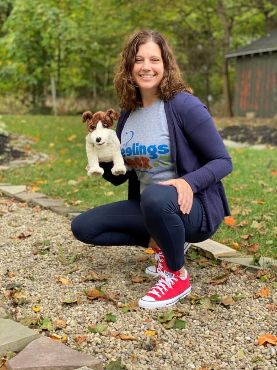 woman crouching outside with a brown and white dog mascot