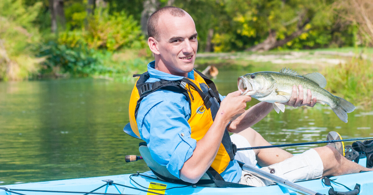 man in kayak holding a caught fish, part of Heroes on the Water