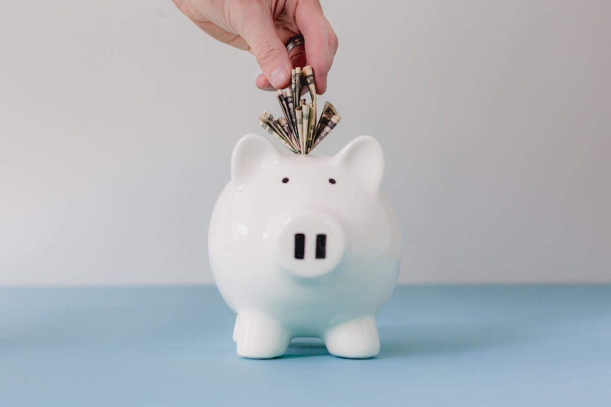 putting money in a white piggy bank to address your financial debt in a healthy way