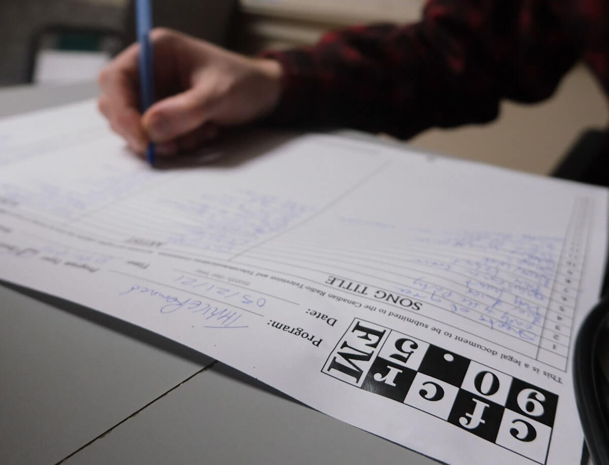 a man's hand on a song list sheet at the saskatoon community radio station