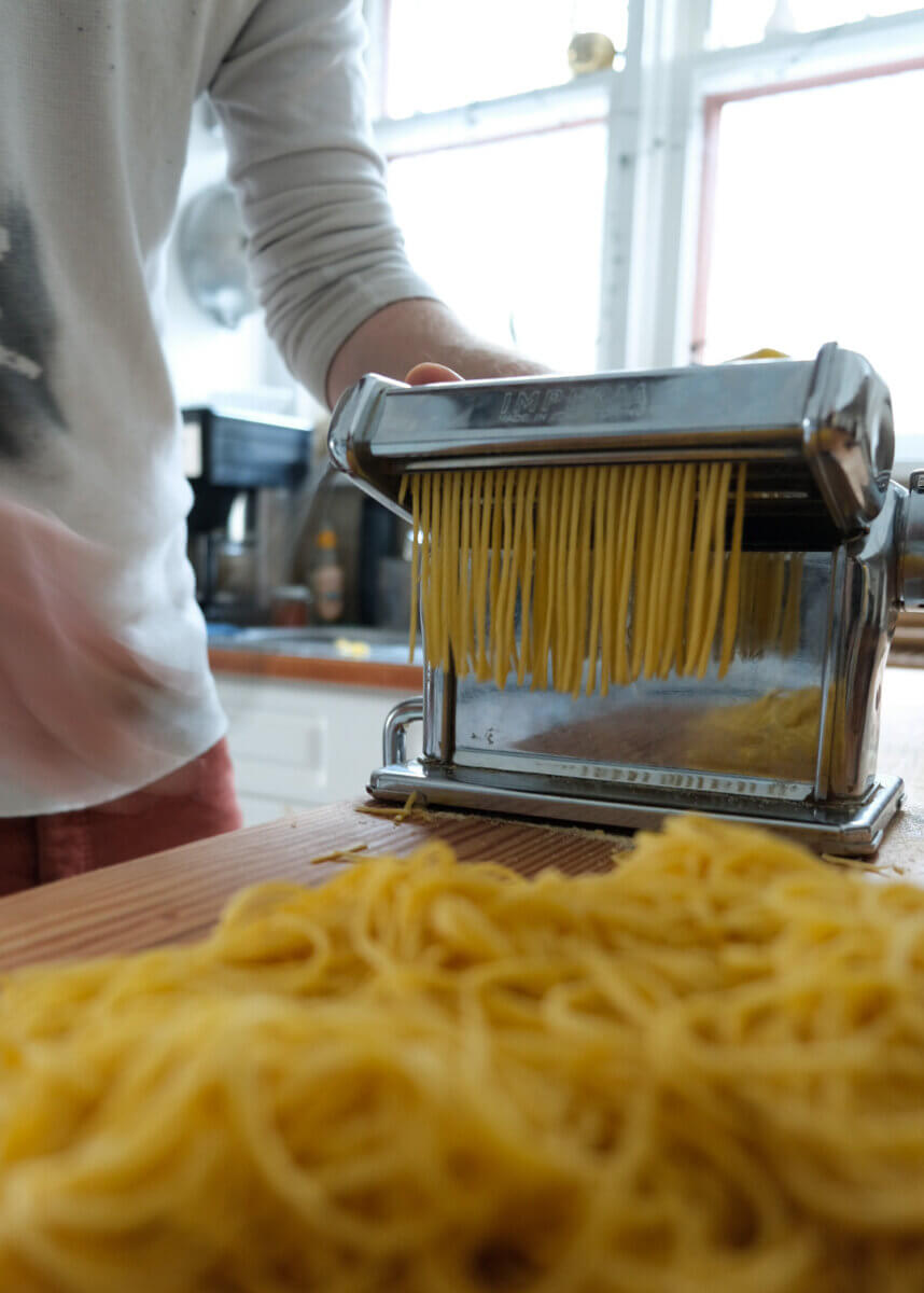 a silver pasta roller producing noodles, a quality piece of secondhand kitchen equipment