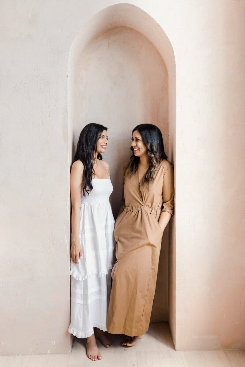 2 women in white and brown long dresses, smiling at each other