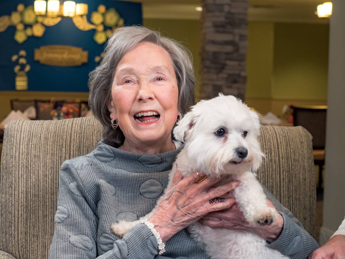 happy elderly woman holding her small white dog while doggies for dementia takes a photo