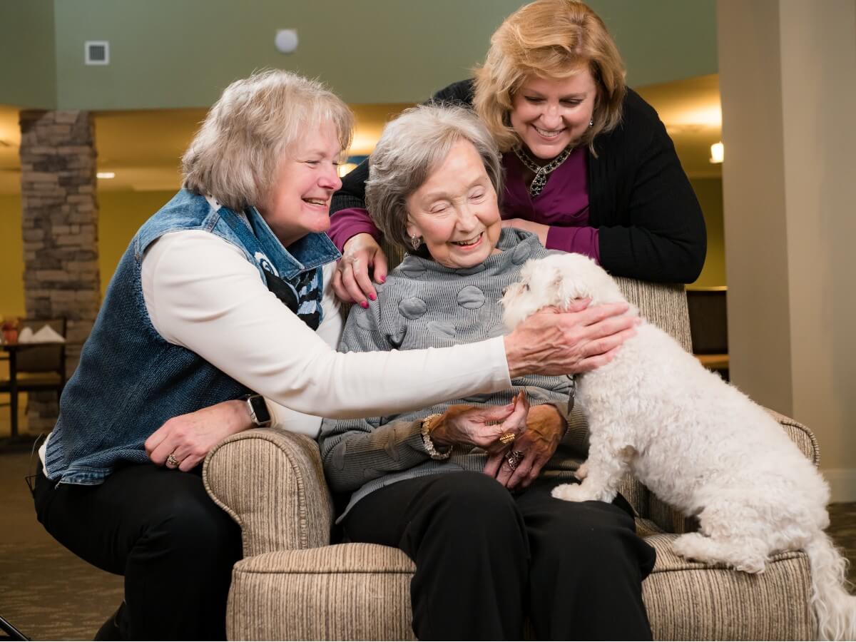 2 women with their mother adoring a small white dog