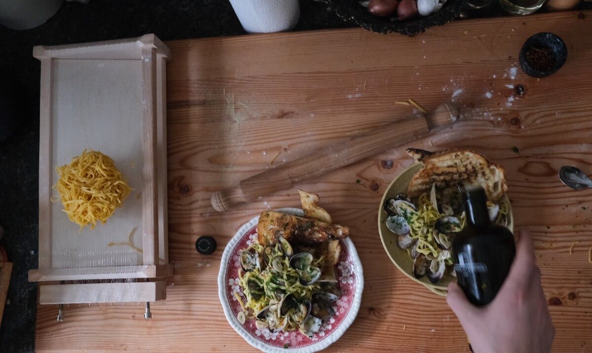 a pasta chitarra and 2 bowls of pasta on a wooden board