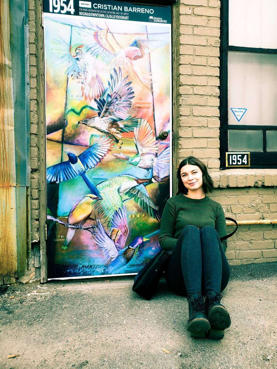 woman sitting beside a mural in Regina's Cathedral community