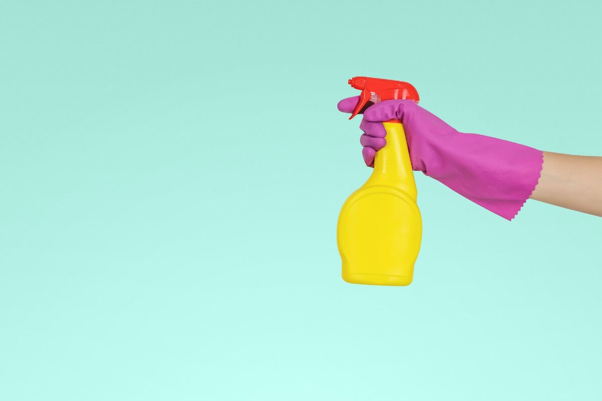 person with pink glove spraying a yellow plastic chemical bottle 