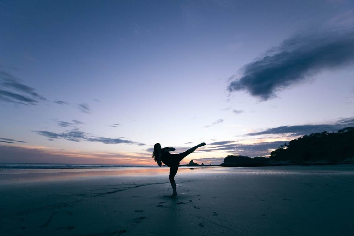 woman kicking on a beach at sunset in a women's self-defense BJJ class  