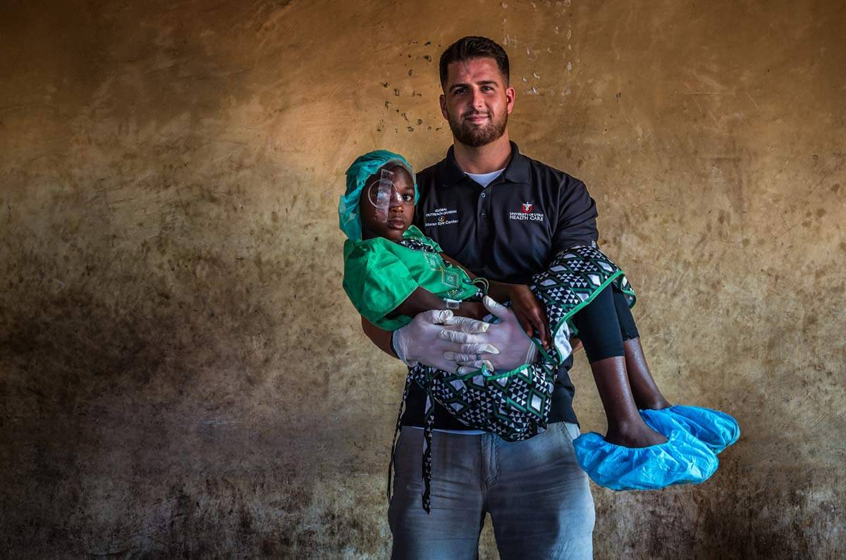 a male doctor holding a young girl  who has been treated for blindness
