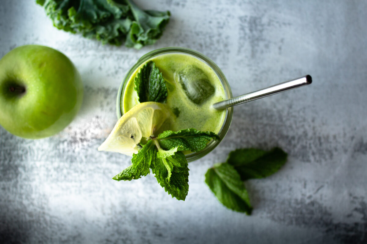 glass of green juice with kale beside green apples