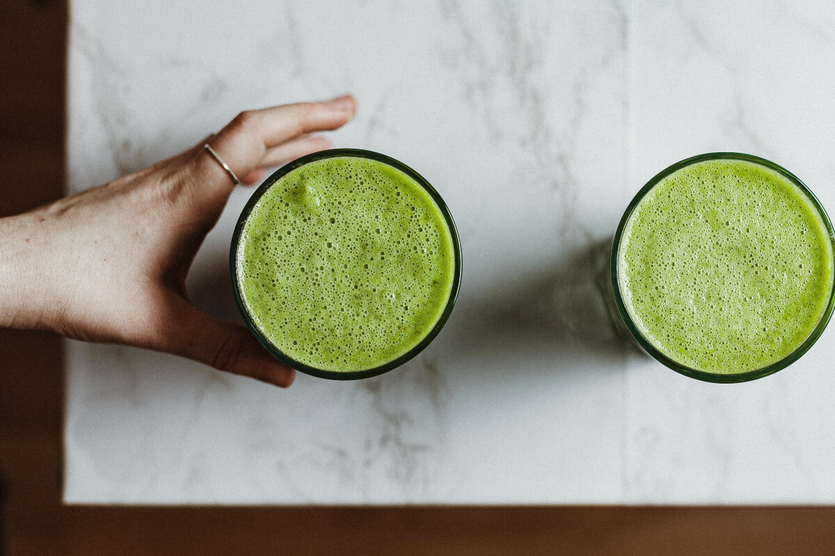 a hand grabbing one of two glasses of green juice