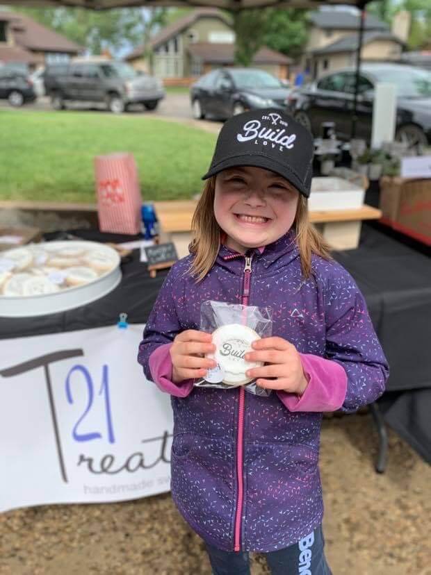 young girl in purple jacket holding a cookie from 21 treats