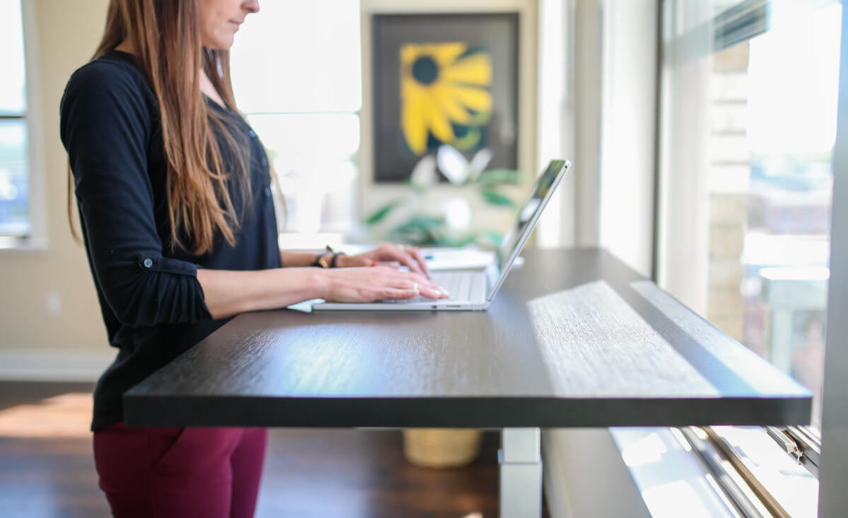 woman working on laptop at standing desk in a bright office