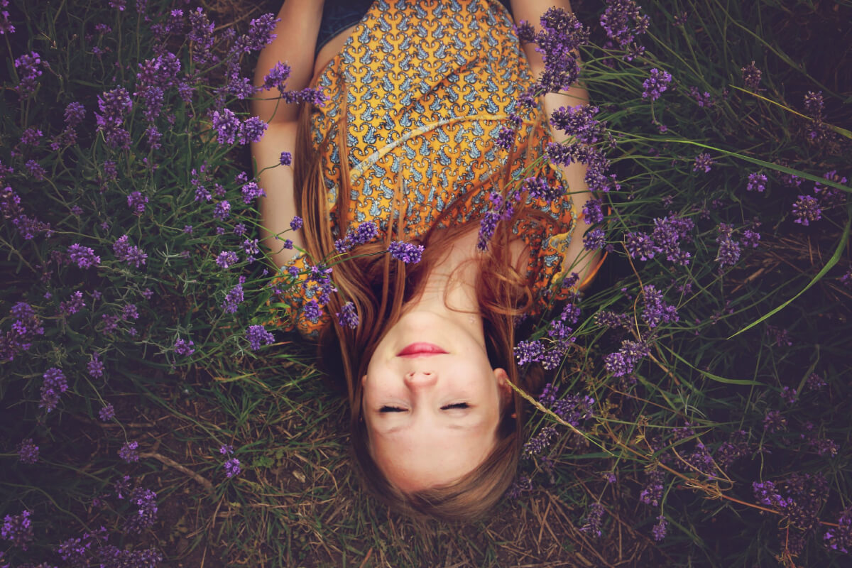 Woman in a yellow floral dress laying in a field of lavender with her eyes closed