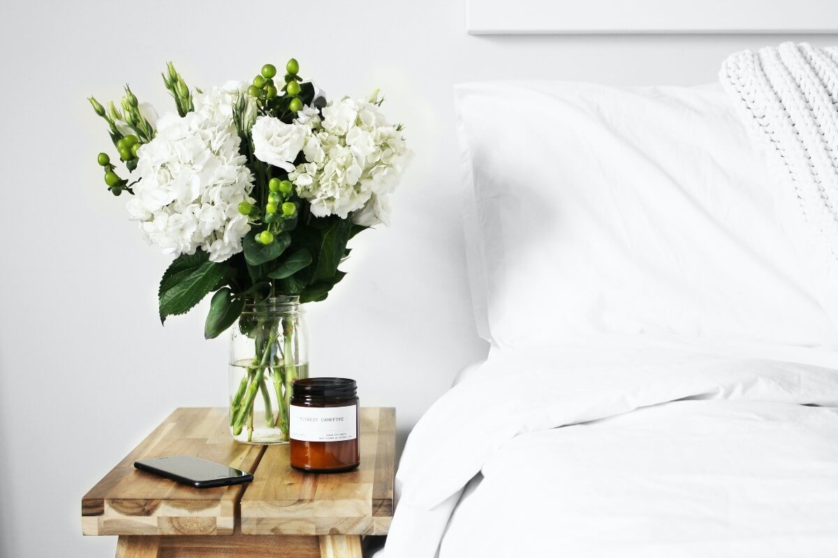 Vase of white flowers and a candle on a wooden nightstand 