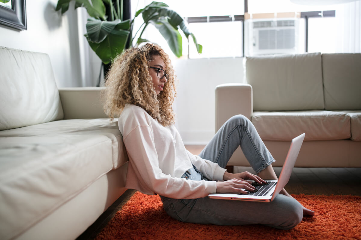 Woman sitting comfortably on her living room rug typing on her laptop 